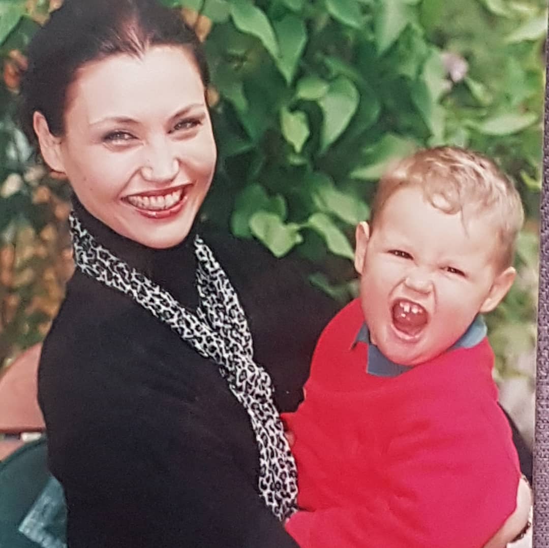 Daniela Nane îmbrăcată într-un pulover negru pe gât, cu o eșarfă cu animal print, ținându-l în brațe pe fiul ei când era mic