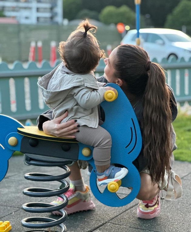 Theo Rose îmbrățișându-și fiul în parc, în timp ce acesta se dă pe un balansoar