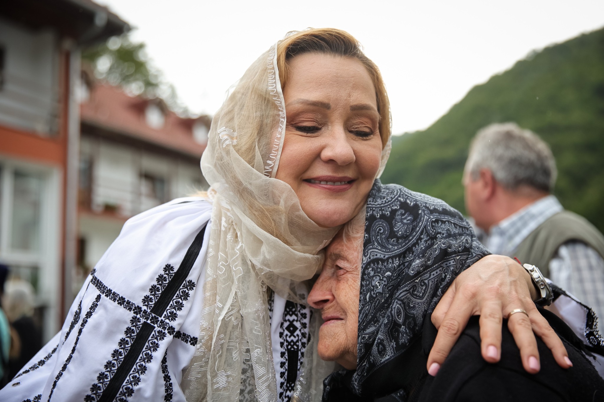 Elena Lasconi în costum popular și cu maramă pe cap, îmbrățișând o bătrână