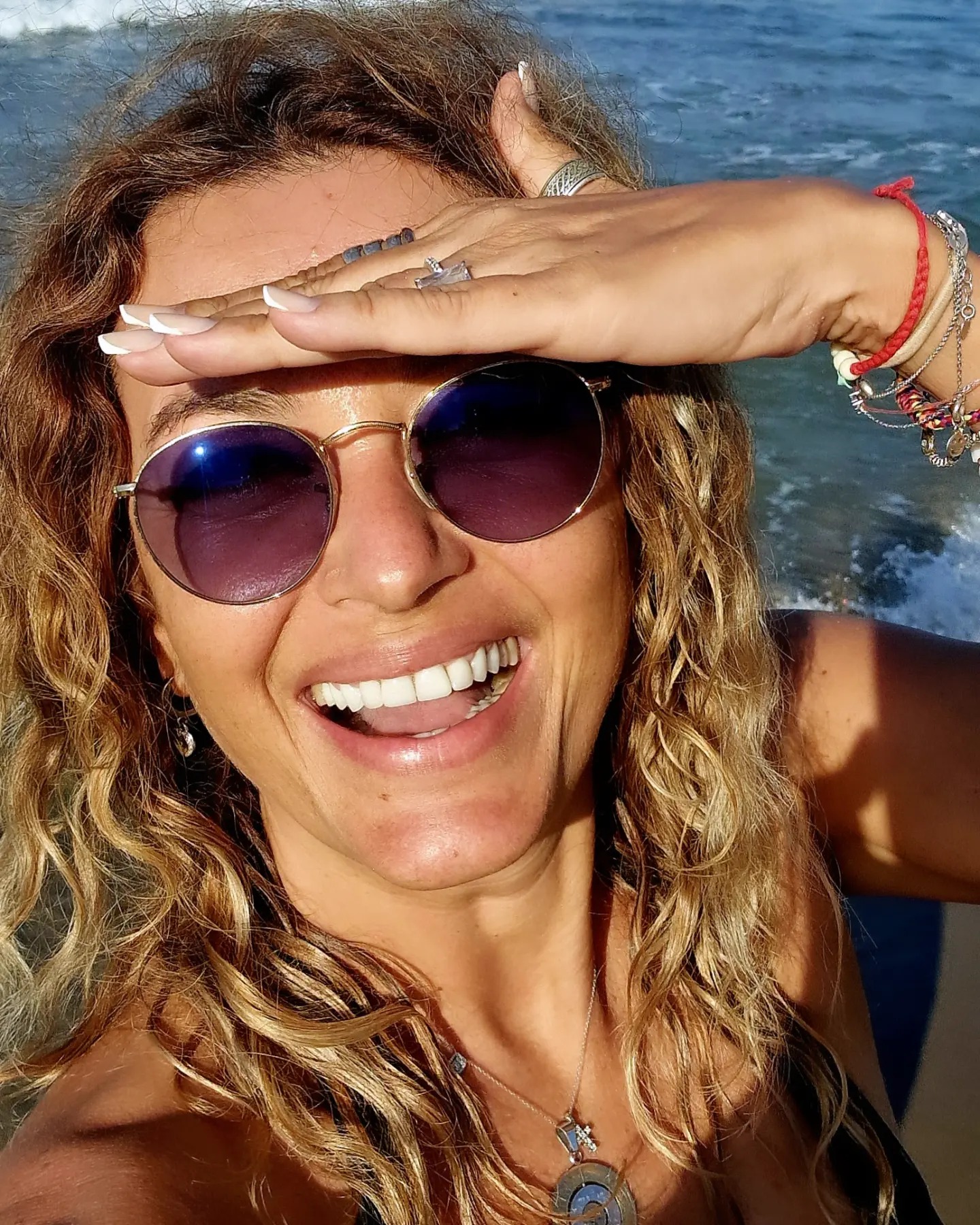 Anca Țurcașiu la mare, în Grecia, ținându-și mâna în dreptul frunții, pentru a se proteja de lumina puternică, în timp ce poartă și ochelari se soare la ochi