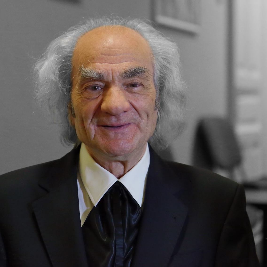 Leon Dănăilă zâmbitor, stând la poză, îmbrăcat în costum negru și cămașă albă