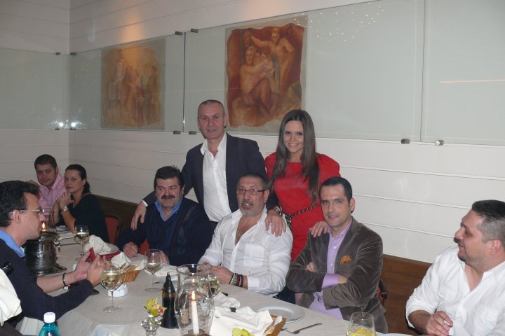 Cristina Șișcanu și George Papari stând lângă masa la care erau așezați Mădălin Ionescu, Serghei Mizil și alți invitați de la ziua afaceristului