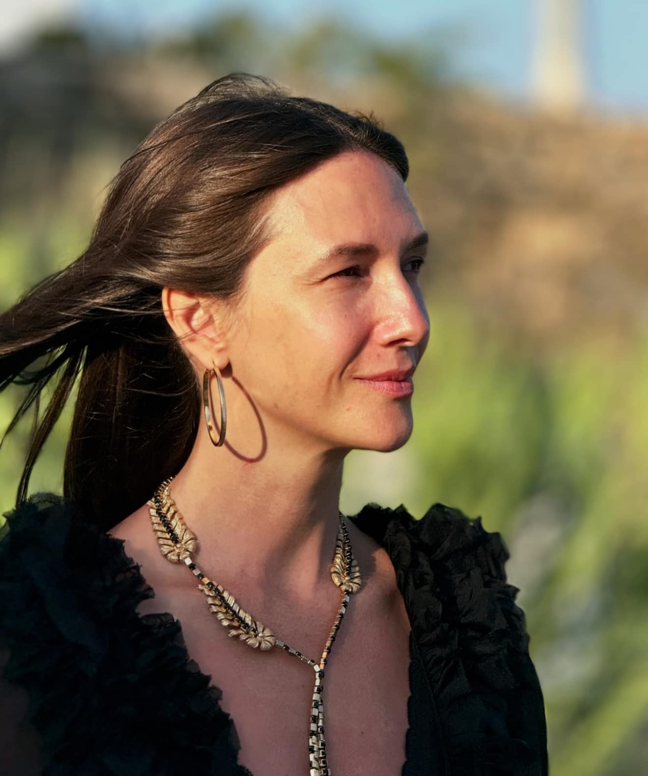 Adela Popescu nemachiată, cu părul în vânt, îmbrăcată în negru, purtând accesorii voluminoase