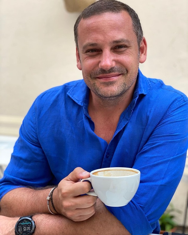 Robert Pongracz într-o cămașă albastră, ținând o ceașcă de cafea în mână