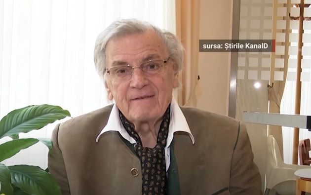 Florin Piersic în clinica din Ungaria în care face recuperare, stând lângă o fereastră și lângă o plantă mare în ghiveci