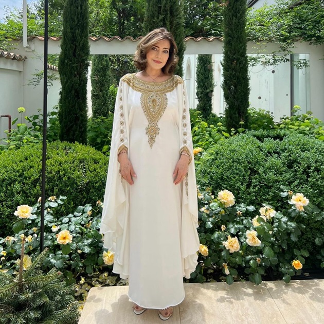 Delia Budeanu într-o grădină plină cu flori, îmbrăcată în rochie albă, lungă
