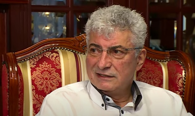 Silviu Prigoană zâmbitor, pe un fotoliu tapițat, în nuanțe de maro, roșu și auriu