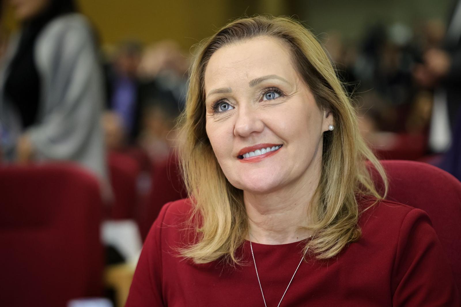 Elena Lasconi zâmbitoare, îmbrăcată în roșu, purtând o cruce mare la gât