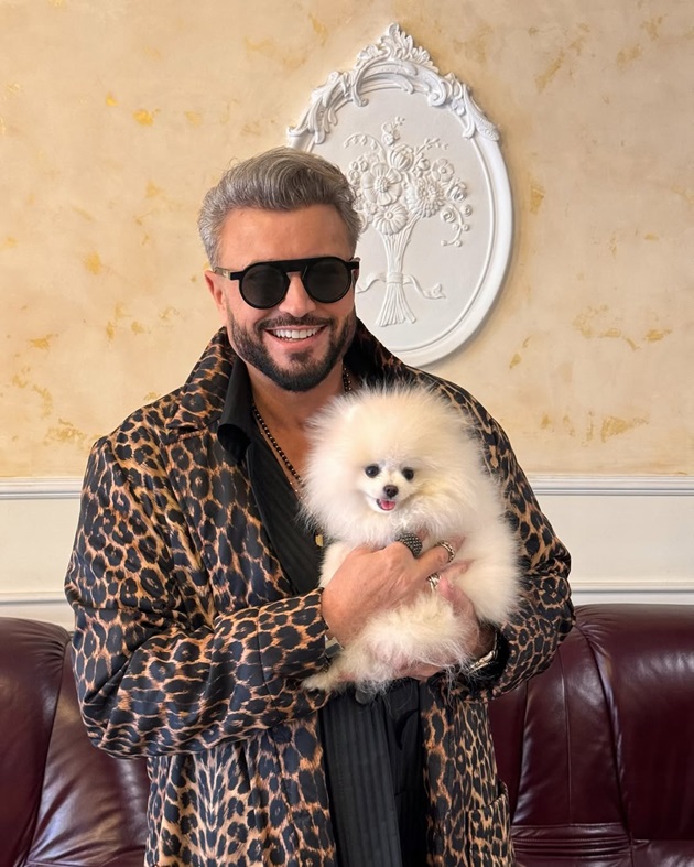 Cătălin Botezatu ținând în brațe un cățel, în timp ce este îmbrăcat într-o jachetă cu animal print