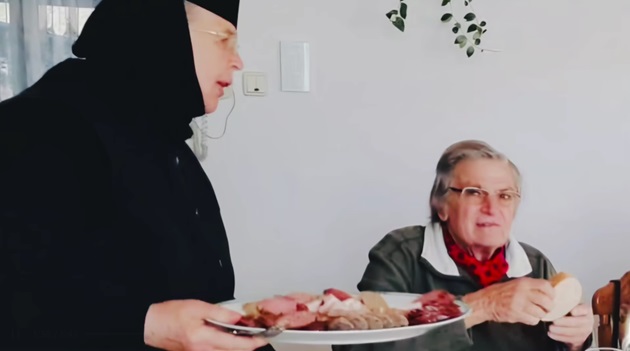 Florin Piersic stă la masă și este servit de o călugăriță de la Mănăstirea Moldovița, unde a fost în vizită
