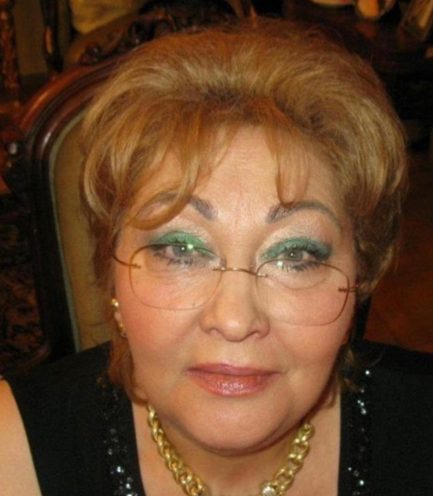 Mărioara Zăvoranu îmbrăcată în negru, purtând un lanț gros de aur la gât, în timp ce era machiată cu verde și purta ochelari de vedere
