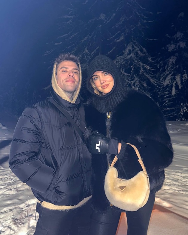 Chiara Ferragni și Fedez îmbrăcați gros, stând lângă un brad acoperit de zăpadă
