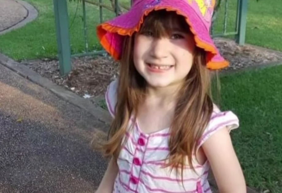 Elizabeth Struhs într-o rochie albă cu dungi roz, purtând pe cap o pălărie colorată