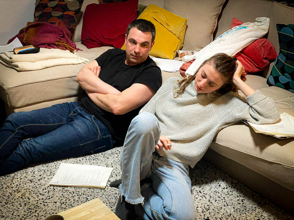 Alexandru Papadopol și Cristina Luca repetând împreună pentru o piesă de teatru, în timp ce stăteau pe covor, lângă canapea