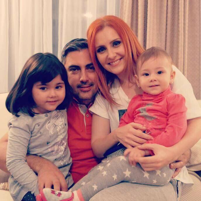 Alina Sorescu și Alexandru Ciucu stând împreună pe canapea și ținându-și în brațe fiicele