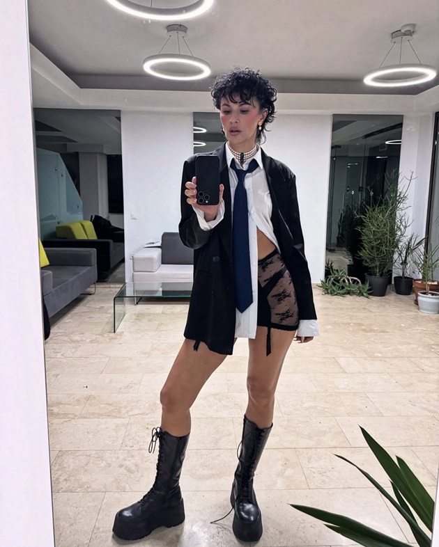 Rux îmbrăcată în pantaloni scurți din dantelă, cămași albă și sacou negru, făcându-și o poză în oglindă