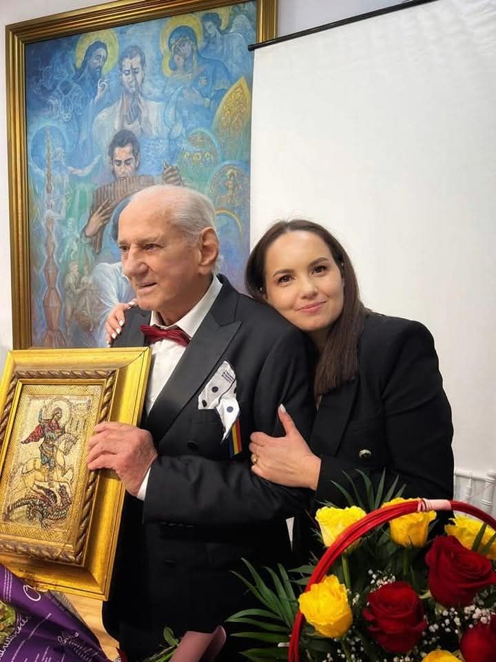 Nicoleta Zamfir îmbrățișându-l pe Gheorghe Zamfir și punându-și capul pe spatele lui, în timp ce acesta ține în mână icoana Sfântului Gheorghe