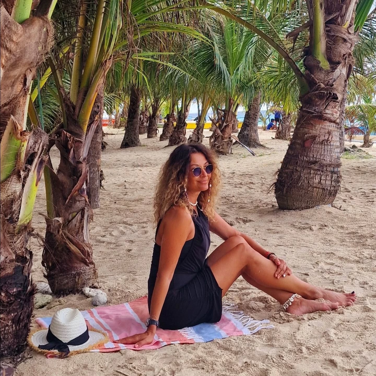 Anca Țurcașiu la plajă, îmbrăcată într-o rochie neagră, stând pe un prosop colorat