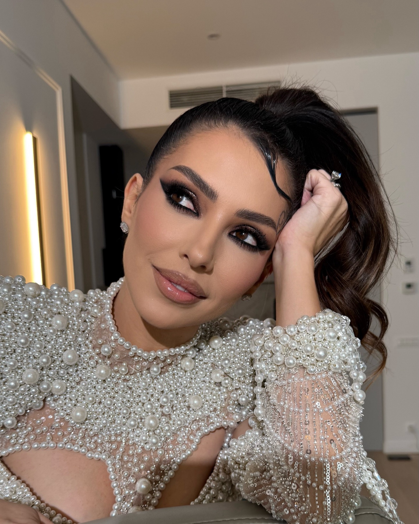 Celia îmbrăcată într-o bluză accesorizată cu multe perle, cu părul prins, în timp ce privește într-o parte