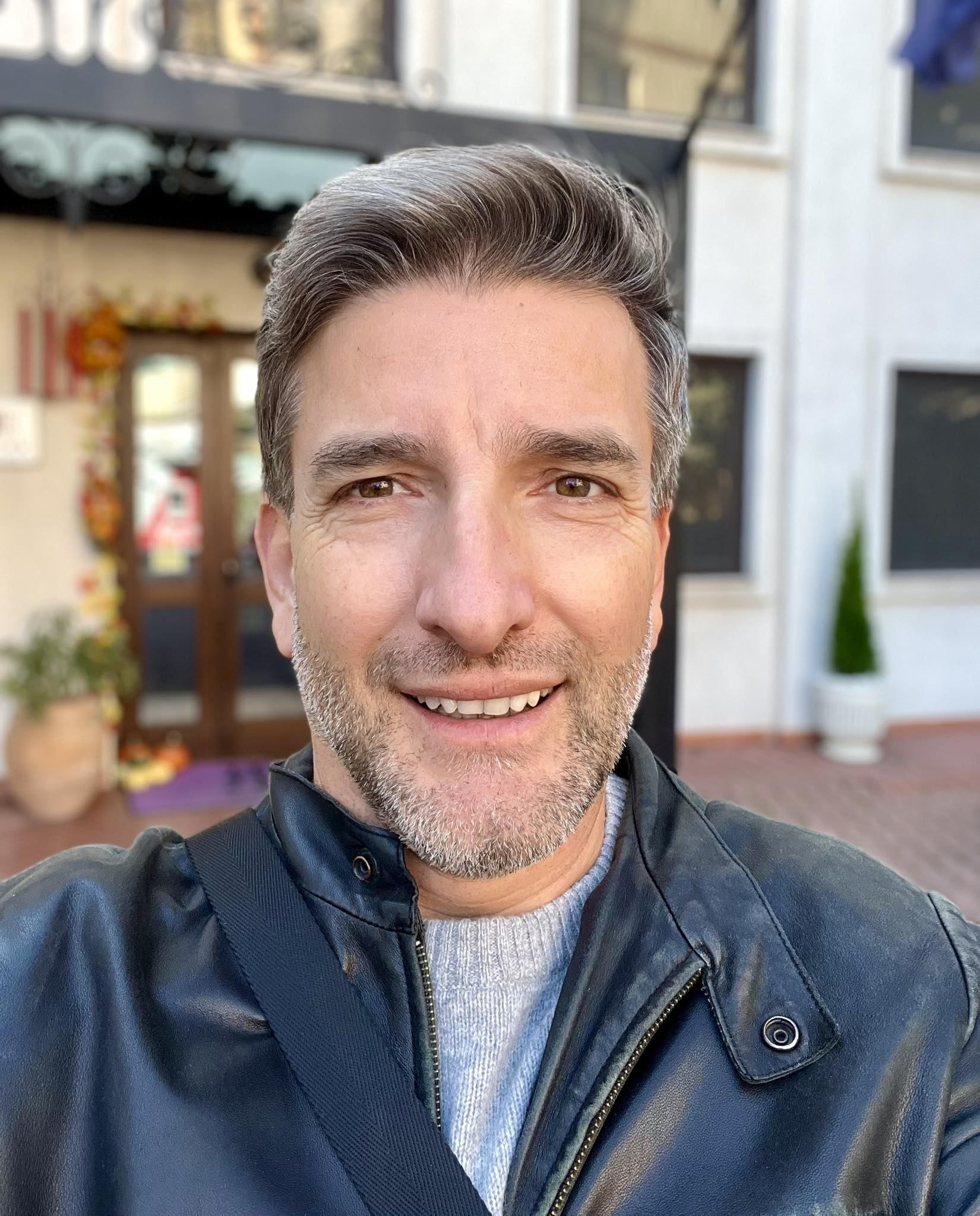Silviu Biriș zâmbitor, în pulover gri și geacă de piele neagră