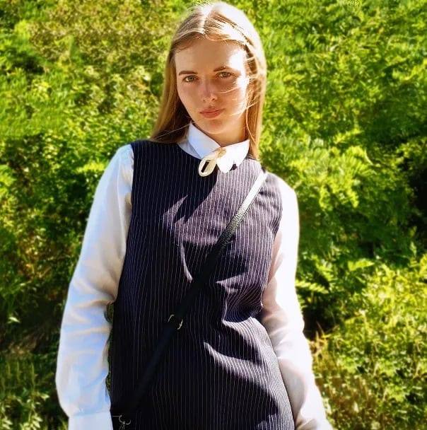 Andreea-Cristiana Oană îmbrăcată în cămași albă și sarafan închis la culoare cu dungi