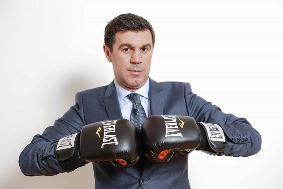 Fostul campion mondial la box, Mihai Leu, îmbrăcat în costum, ținând mănușile de box în mâini