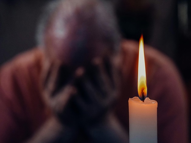 Persoană tristă, care stă lângă o lumânare și se ține cu mâinile de cap
