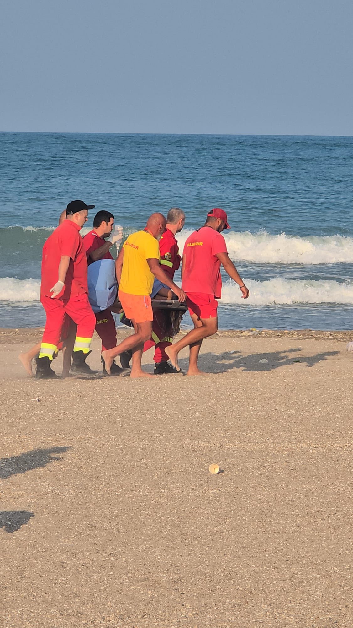 Salvamarii din Costinești și medicii de pe echipajele SMURD transportând-o pe femeia de 21 de ani către elicopterul care a dus-o la spital