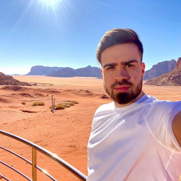 Anghel Vlad Antonio îmbrăcat într-un tricou alb, făcându-și un selfie undeva în deșert