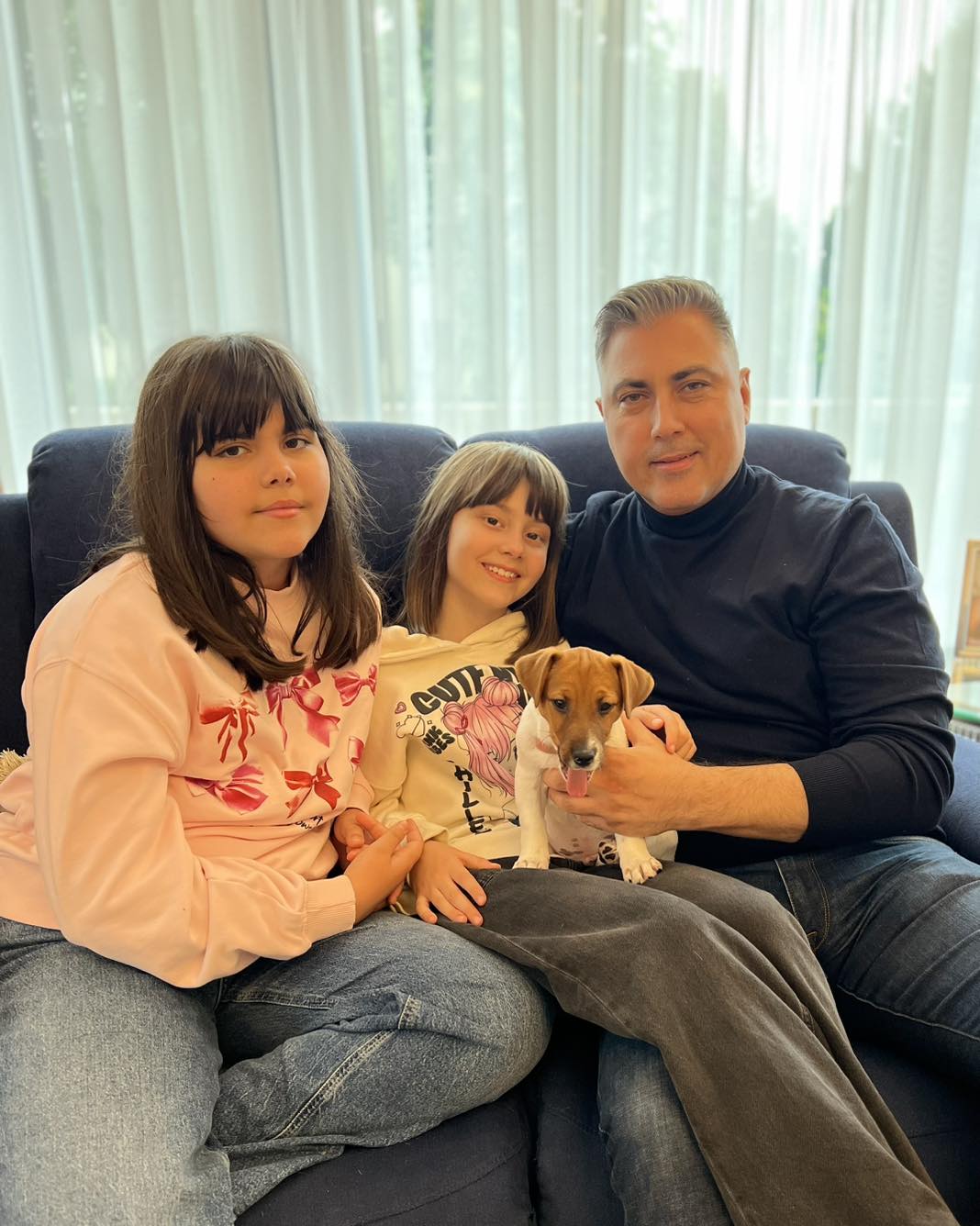 Alexandru Ciucu stând pe canapea, alături de fiicele sale, Carolina și Raisa, care țin în brațe un cățel