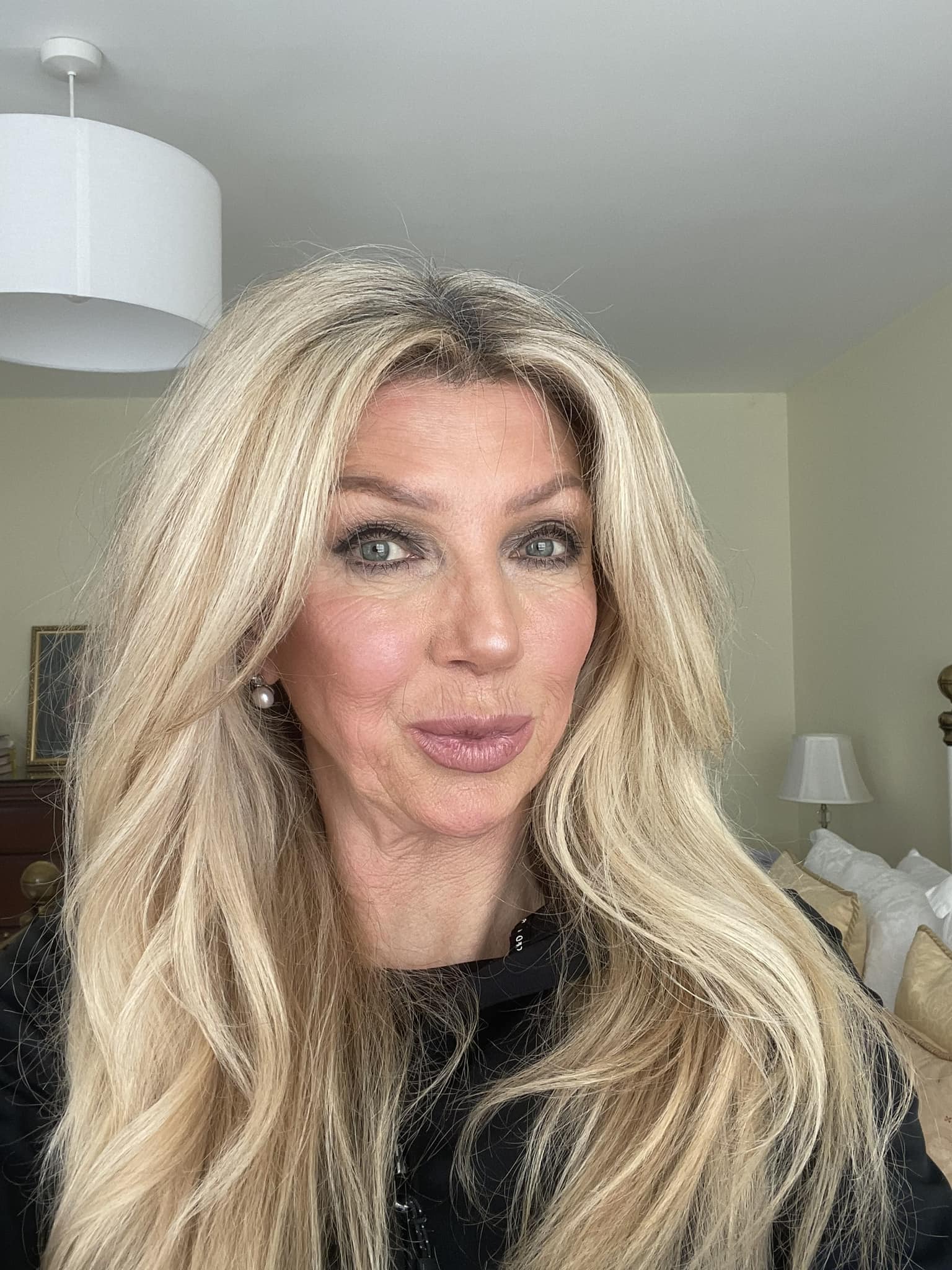Kate Shemirani, fosta asistentă medicală, îmbrăcată în negru, cu părul lung și blond coafat sub formă de bucle lejere