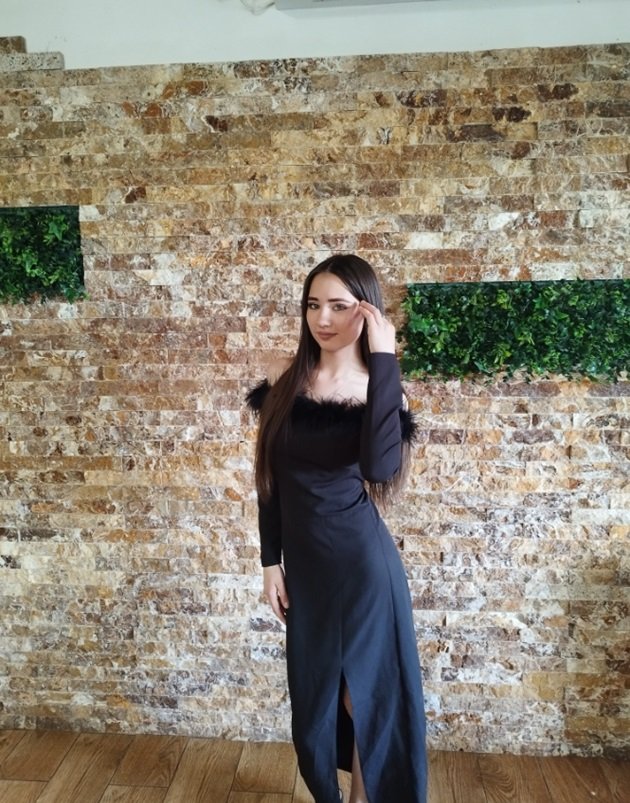 Adelina Teșu îmbrăcată într-o rochie lungă, neagră, cu umerii goi, cu pene în jurul bustului și cu crăpătură pe picior