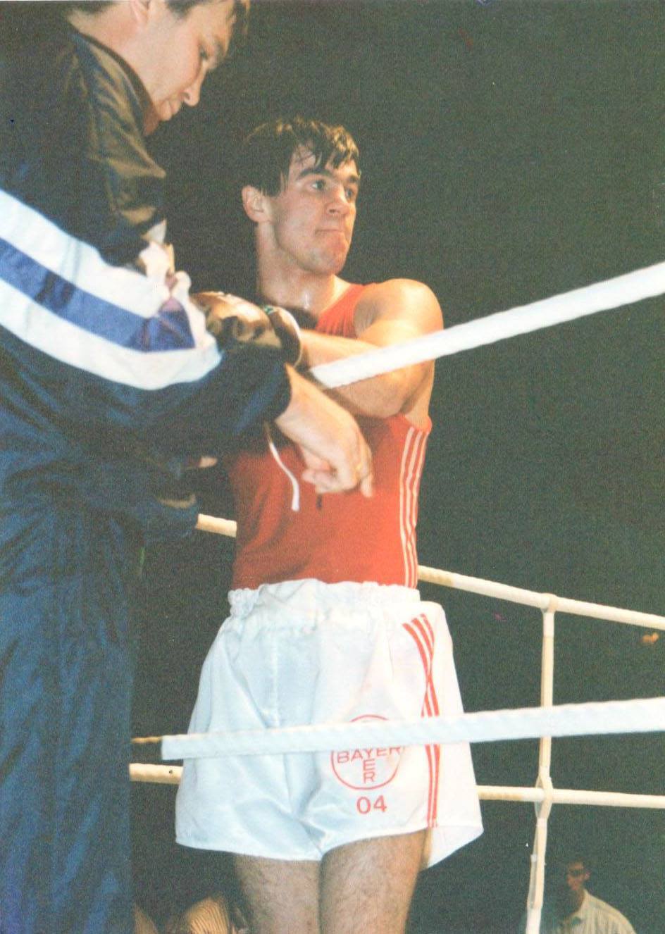 Mihai Leu în ring, în timpul unui meci, îmbrăcat în pantaloni scurți albi și maiou roșu