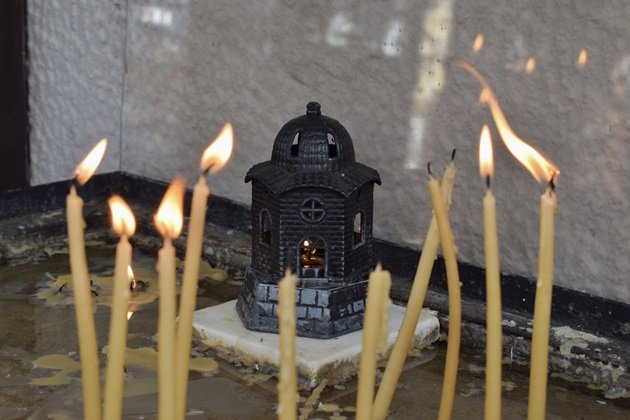 Lumânări galbele care ard în jurul unei candele în formă de biserică, în interiorul căreia se află o altă lumânare