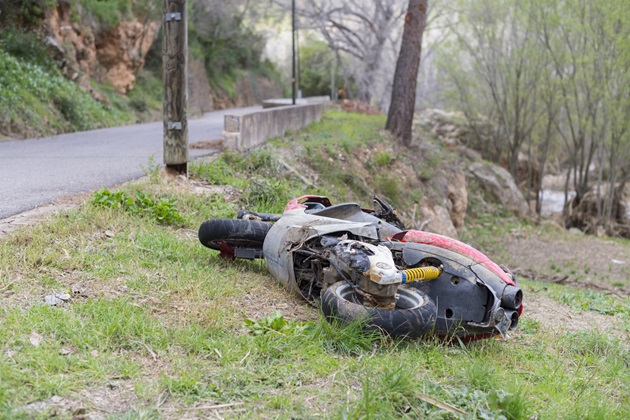Motocicletă trântită la pământ pe marginea drumului, într-o zonă împădurită