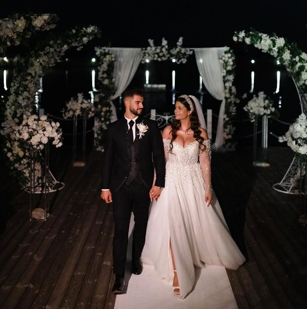 Denisa și Iancu Sterp în ziua nunții, îmbrăcați în mire și mireasă, într-un decor realizat cu numeroase flori albe