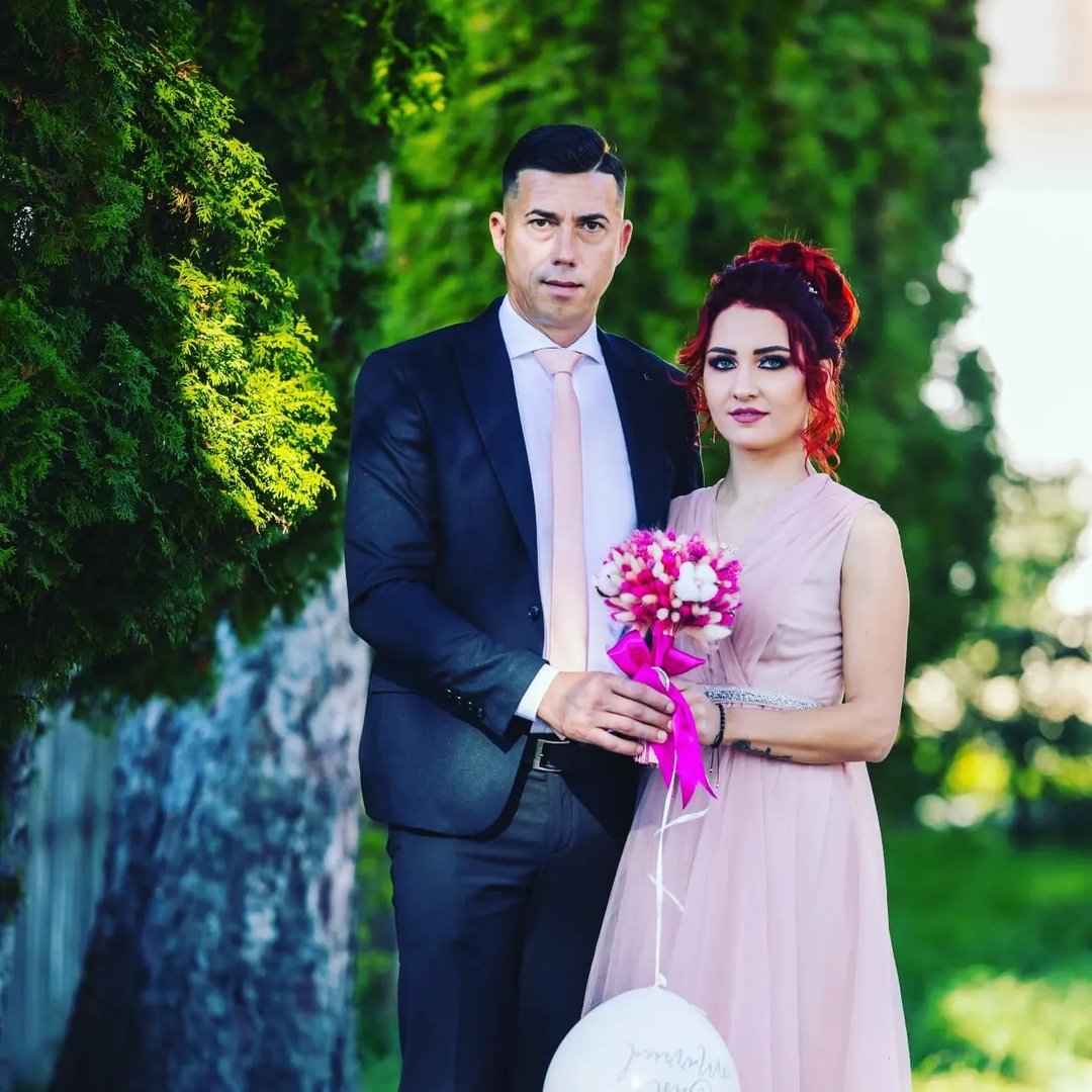 Luiza Bănulescu într-o rochie lungă roz, ținând un buchet în mână, stând alături de soțul ei, în ziua cununiei
