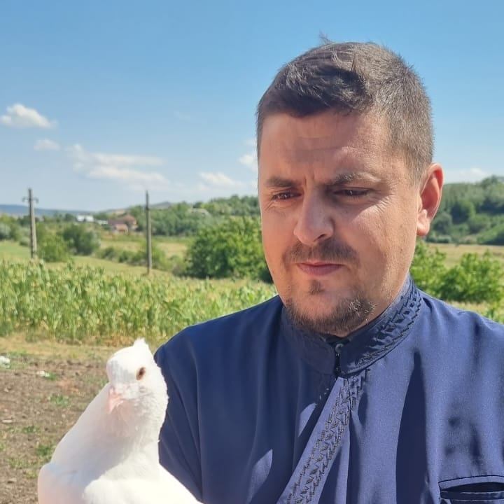 Părintele Ioan Mihai Măriuța, îmbrăcat în straie preoțești, ținând un porumbel în mână