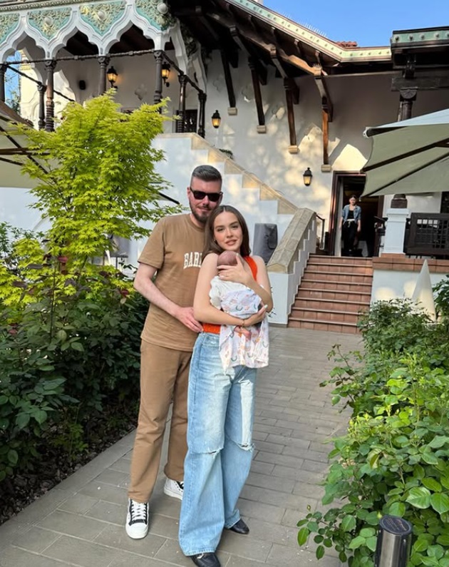 Virgil Boglea cuprinzând-o în brațe pe Mara Boglea care îl ține în brațe pe fiul lor, Carol, în curtea unui restaurant