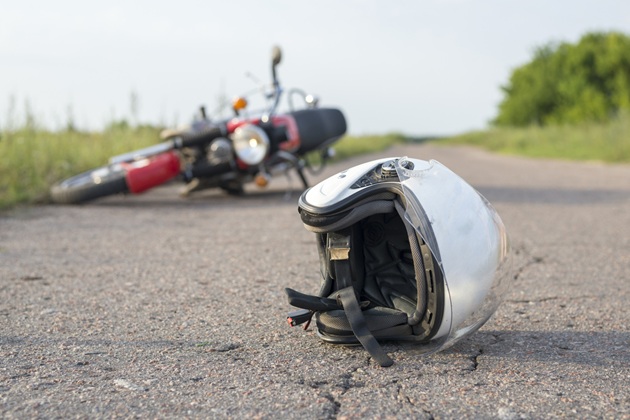 Motocicletă răsturnată și cască de motociclist pe asfalt, în urma unui accident