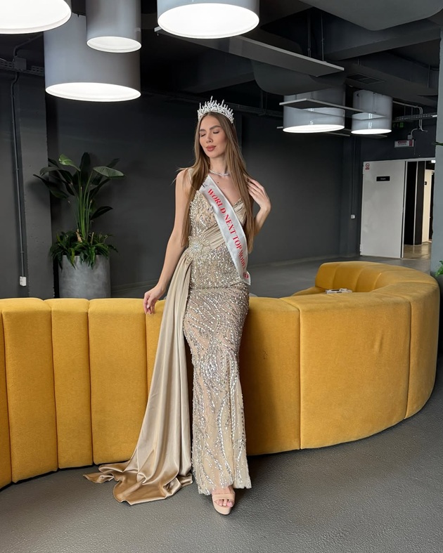 Olga Guțanu, iubita lui CRBL, într-o rochie lungă se seară, de culoare bej, purtând pe umeri o banderolă de la un concurs de miss