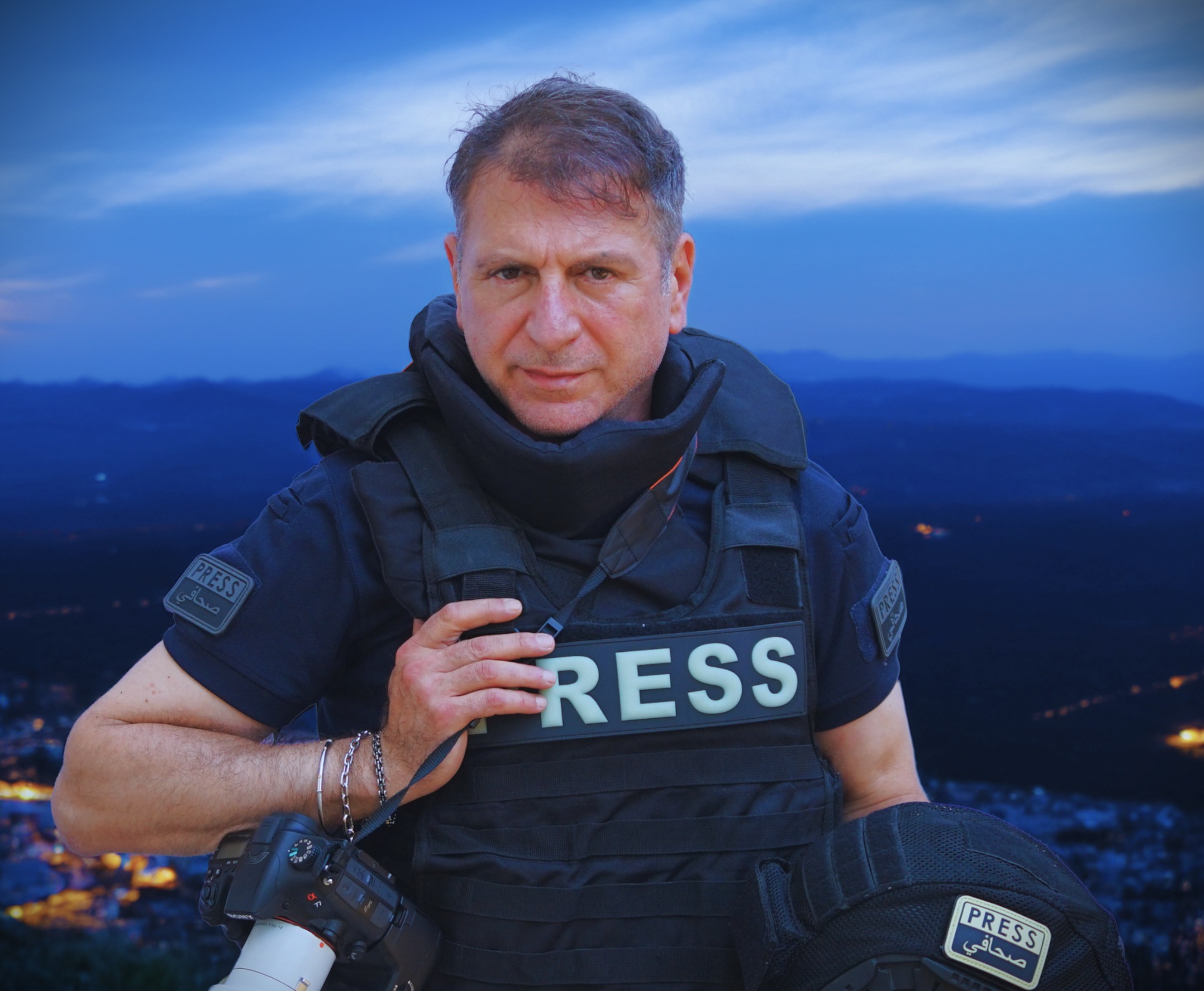 Christian Sabbagh îmbrăcat într-un echipament de război pe care scrie „press”, ținând în mână un aparat de fotografiat