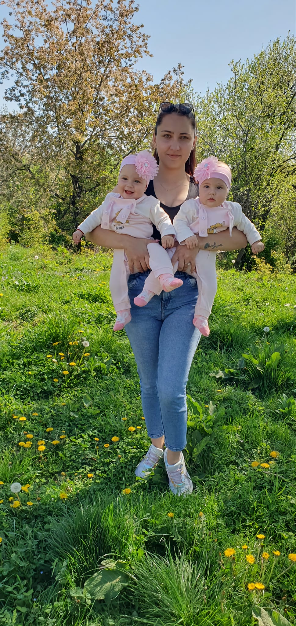 Luiza Bănulescu în natură, ținându-și în brațe gemenele, îmbrăcate la fel, cu bentițe roz pe cap