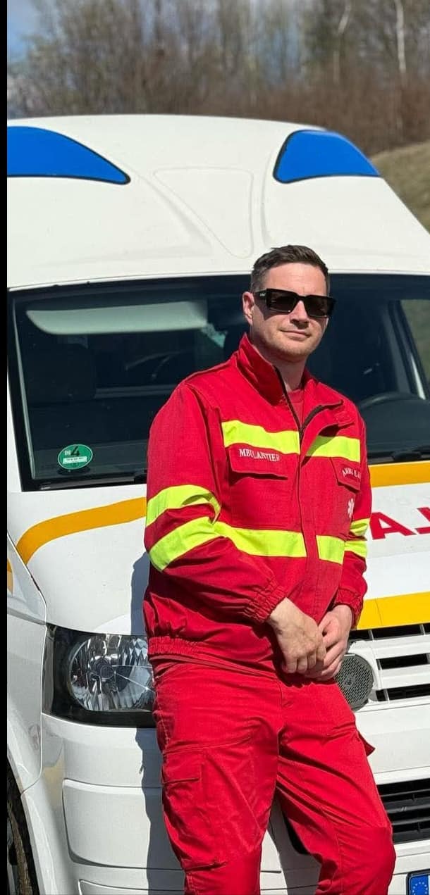Andrei Haureș, asistent medical în Suceava, îmbrăcat în uniforma de serviciu, sprijinindu-se de ambulanța pe care lucra