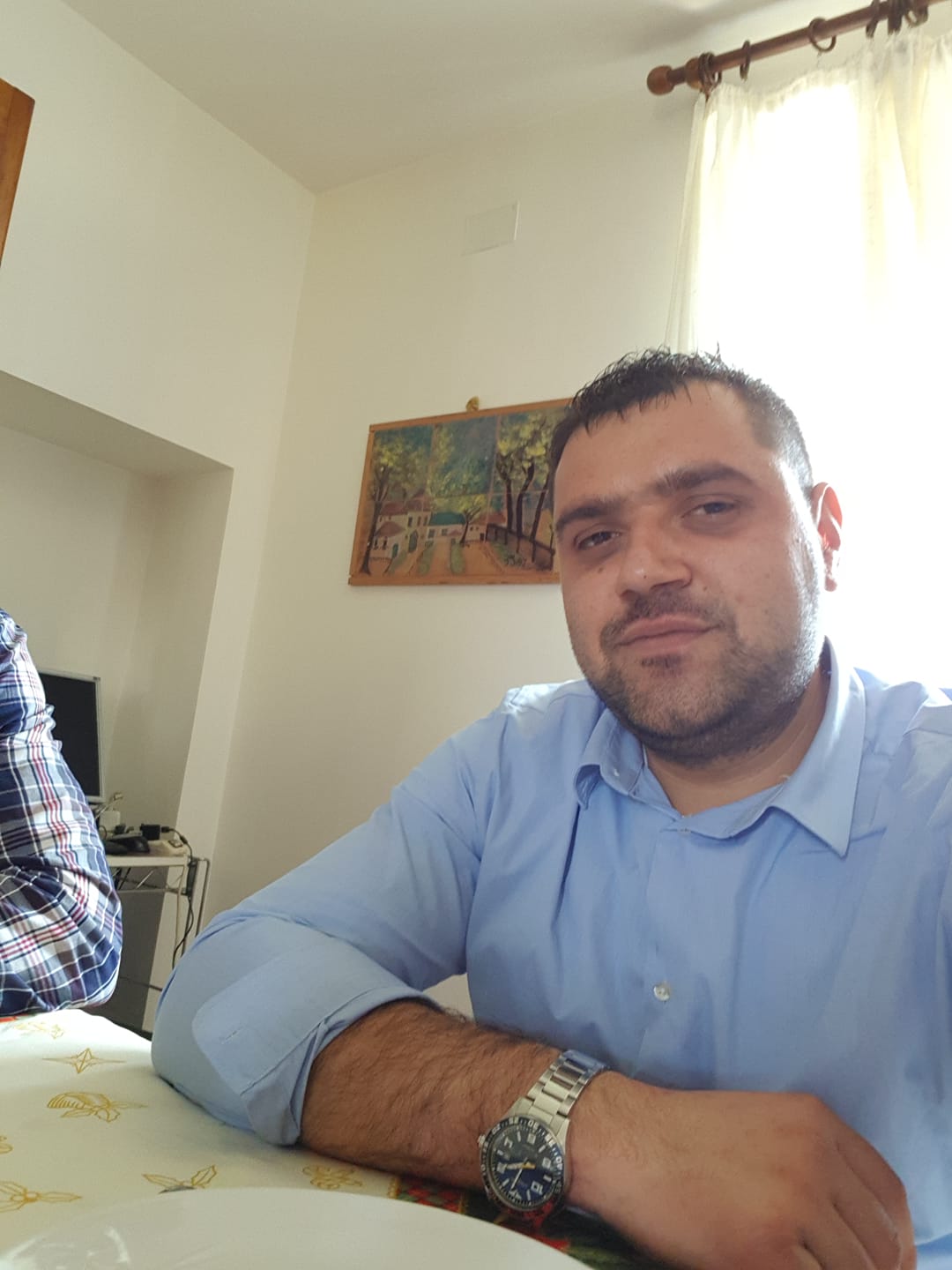 Valentin Ionuț Crișan, românul ucis de cumnatul său în Italia, stâns la o masă, îmbrăcat în cămașă, ținând mâna pe masă și arătându-și ceasul