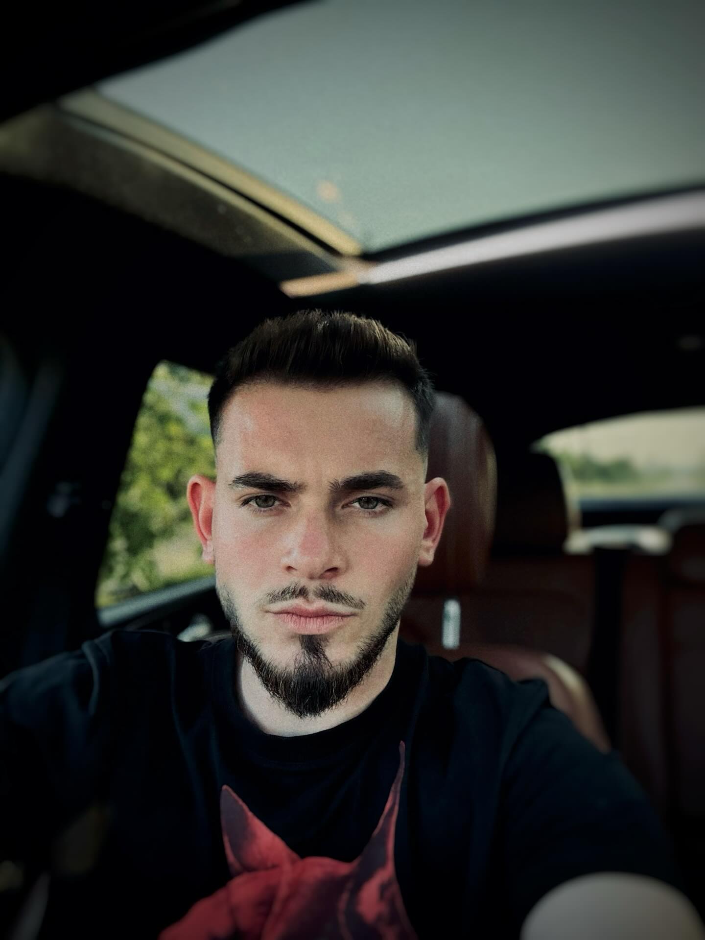 Robert Miloș făcându-și un selfie în mașină îmbrăcat într-un tricou negru cu roșu