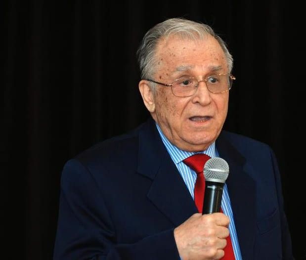 Ion Iliescu vorbind la microfon în fața unui public, îmbrăcat într-un costum închis la culoare, cu o cămașă albă cu dungi albastre și cravată roșie