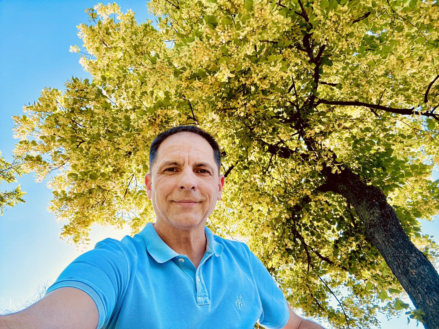 Dan Negru într-un tricou bleu, făcându-și un selfie sub un copac impresionant cu frunze îngălbenite