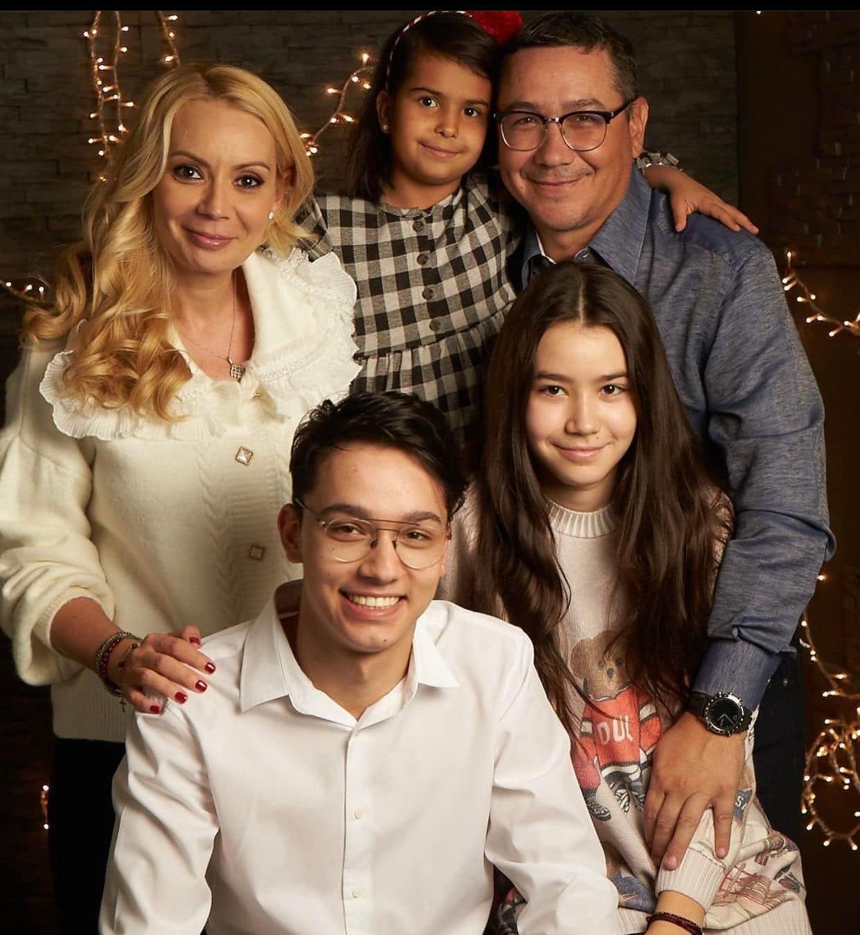 Victor Ponta și Daciana Sârbu cuprinzându-și cei trei copii în brațe, în cadrul unei ședințe foto de Crăciun, cu o instalație în fundal
