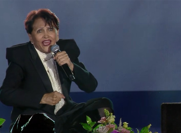 Dida Drăgan cântând așezată pe scena Festivalului Mamaia 2025, în costumul negru bărbătesc care a consacrat-o